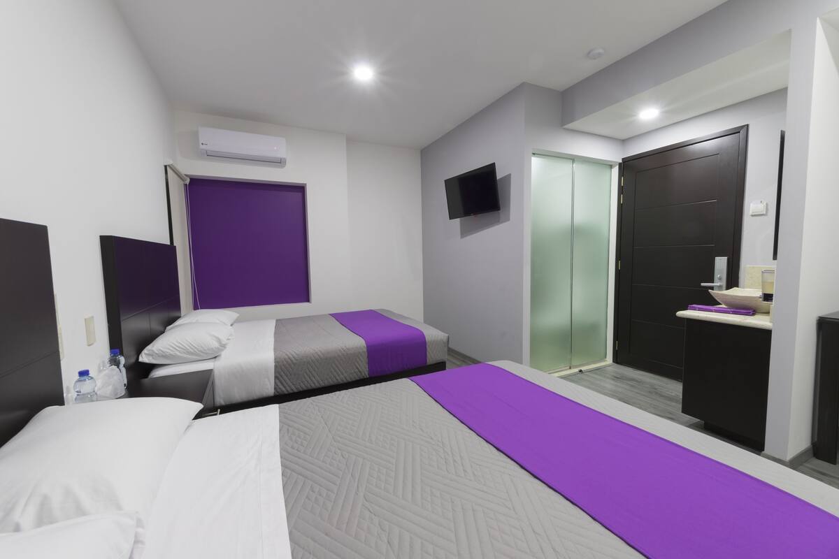 Una habitación de hotel moderna con dos camas, televisión, armario y baño.