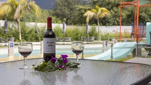 Una mesa con una botella de vino y dos copas, con una piscina y follaje de fondo.