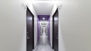 Un pasillo moderno de hotel con piso de madera gris, paredes blancas y detalles morados.