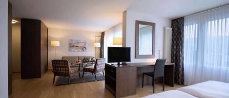 A hotel room with a large bed, a desk with a TV, a chair, a sofa, and a view of the outdoors through the window.