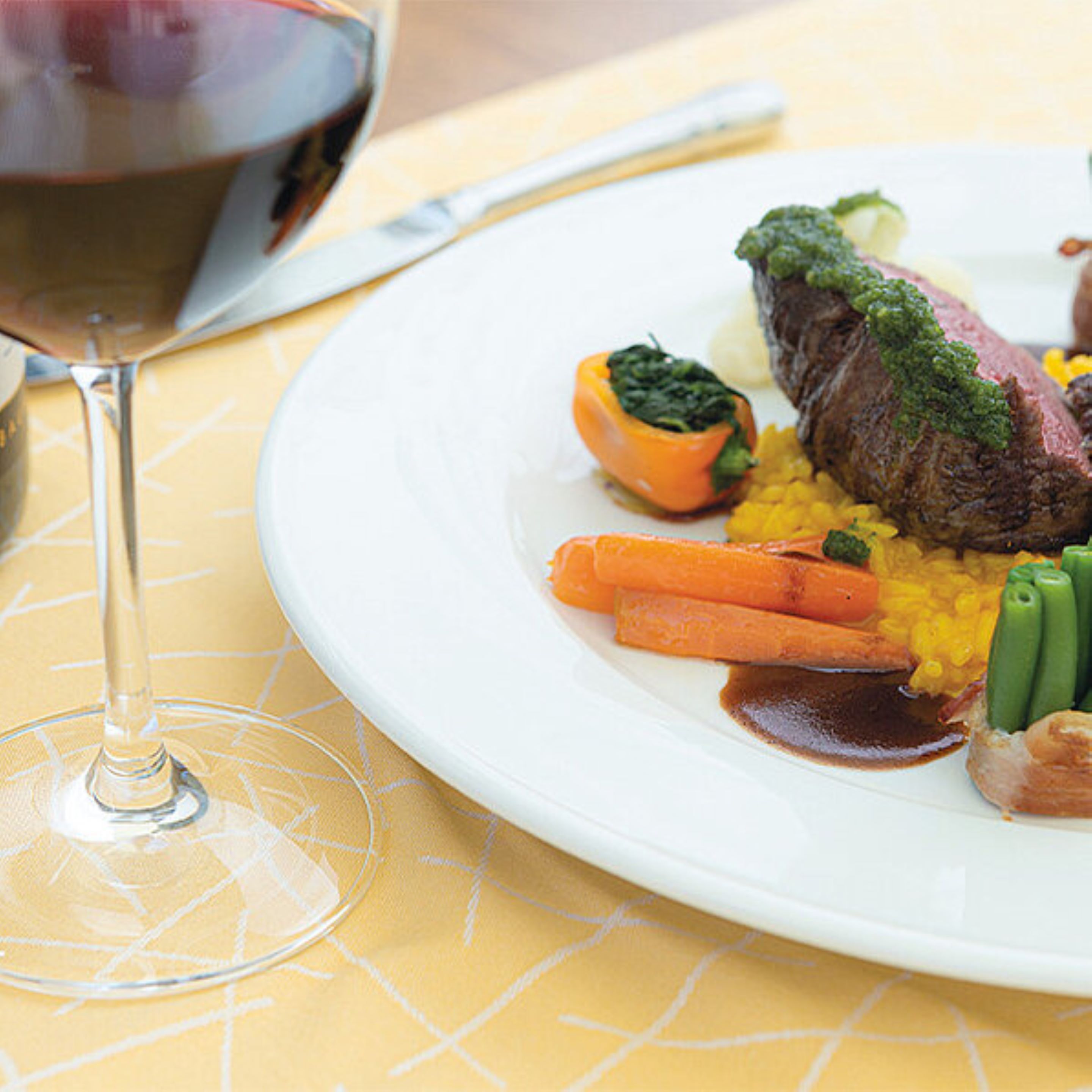A plate of food with a glass of red wine on a yellow tablecloth.