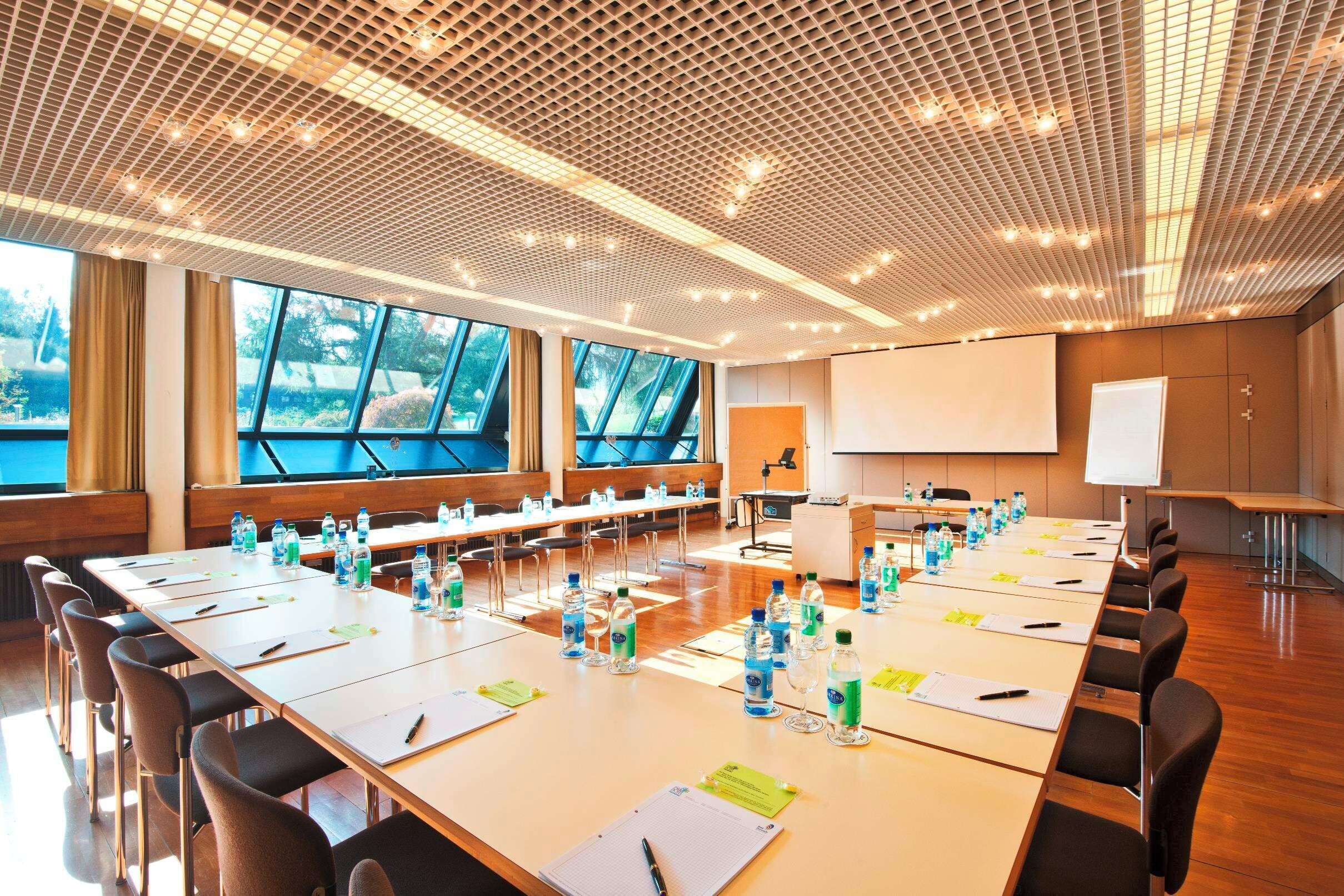 A conference room with long tables, chairs, water bottles, and a projector screen.