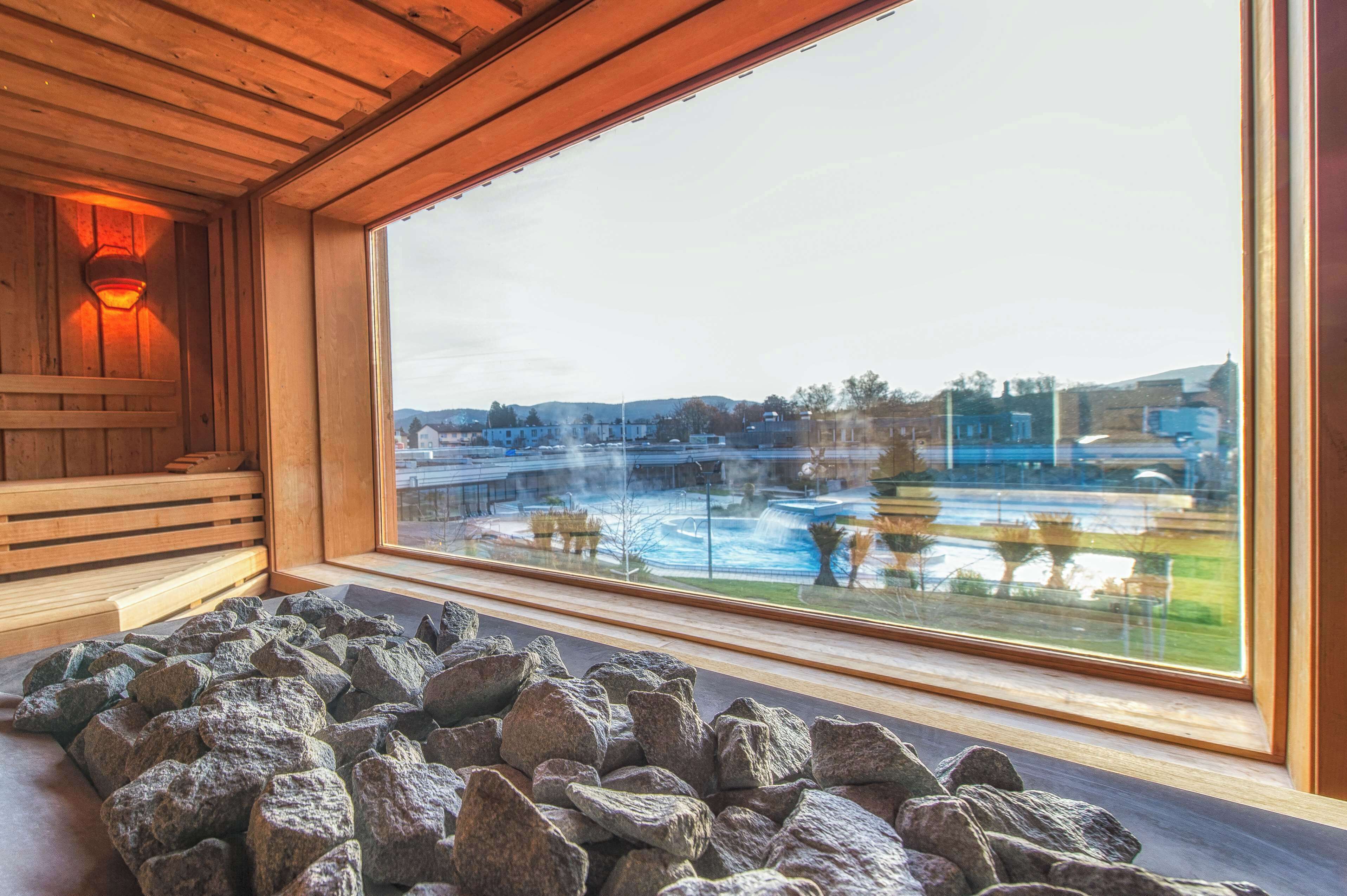 A sauna room with a large window, wooden benches, and a stone floor.