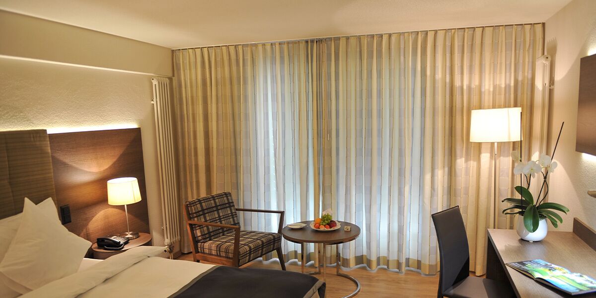 Habitación de hotel con cama, una silla, una mesita con fruta, una lámpara y una planta.
