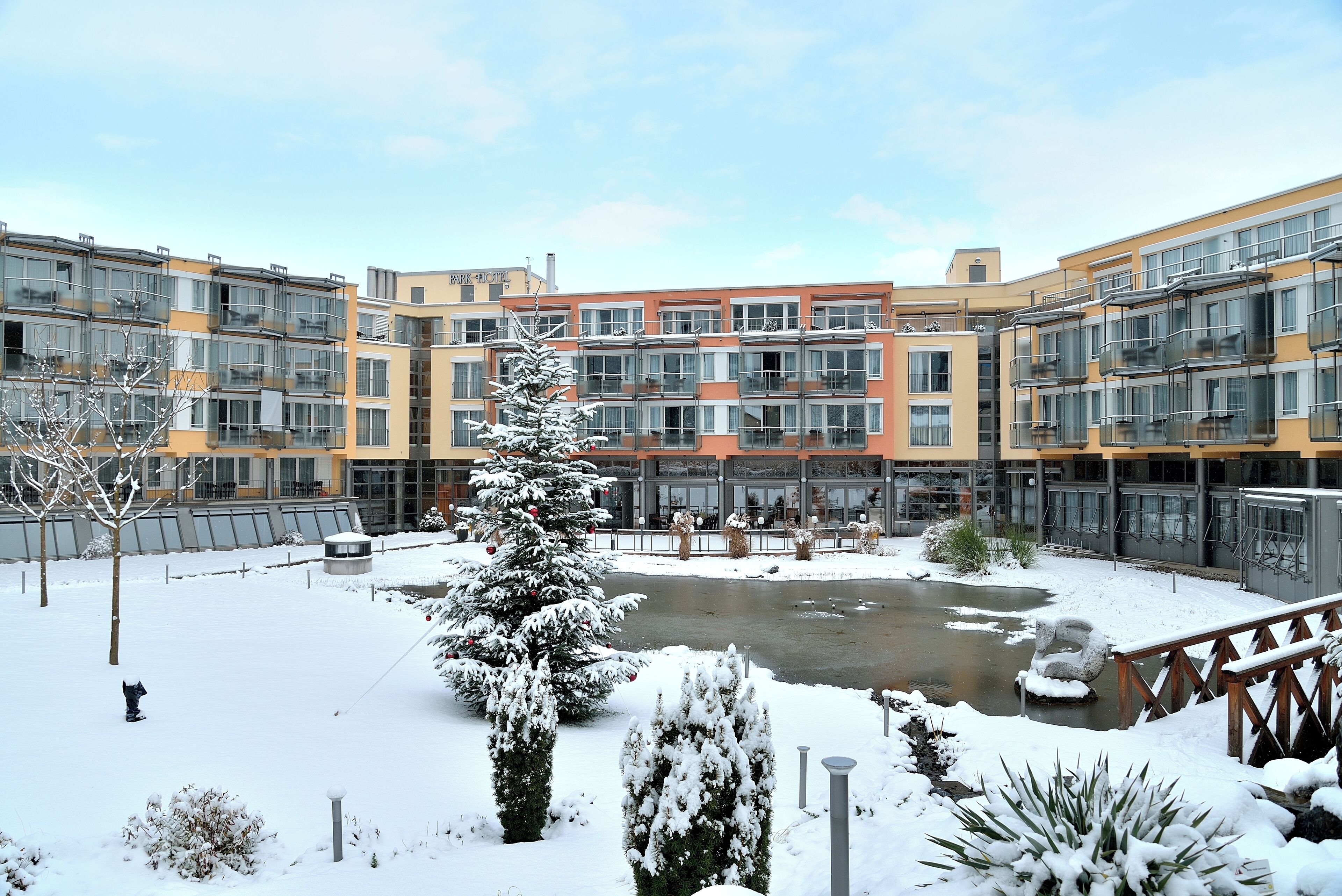A multi-story residential building with balconies, a central courtyard with a water feature, and snow-covered vegetation.