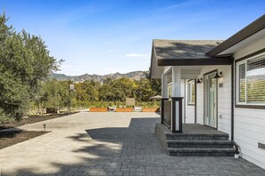 A residential house with a paved driveway, a front porch, and a view of mountains in the background. - Vineyard Villa (Calistoga)