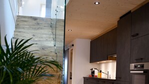 Eine moderne Küche mit dunklen Schränken, einem Edelstahlbackofen und einer Holztreppe, die in eine obere Etage führt.