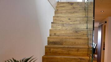 A wooden staircase with glass railings leading to a room with a white wall and a plant on the landing.