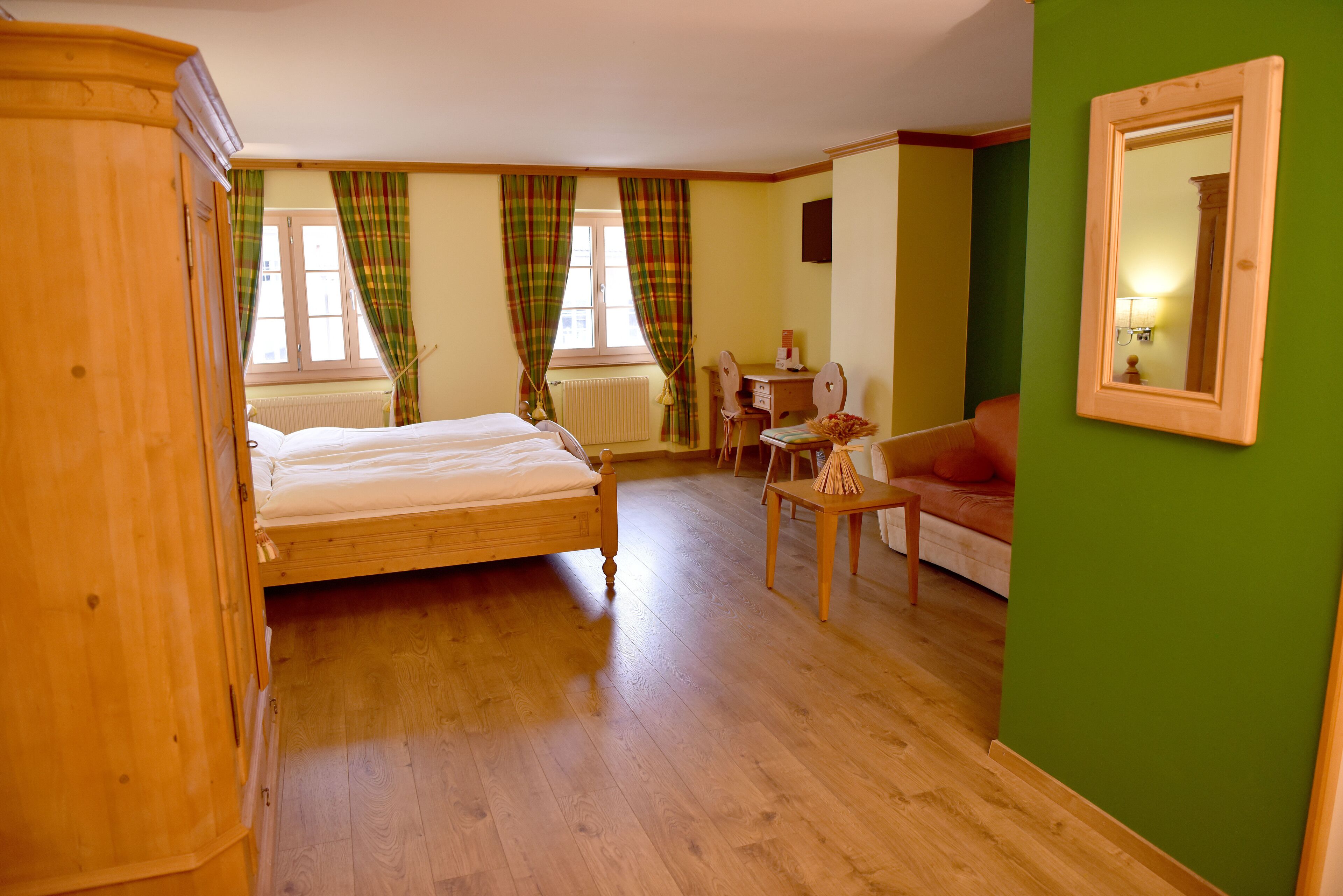 Un dormitorio con una cama de madera, un armario de madera, una pared verde y un espejo.