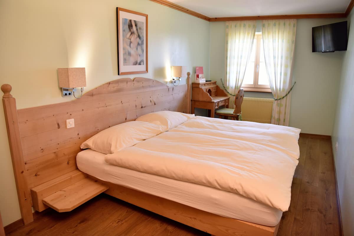 A room with a wooden bed, a desk, a chair, a radiator, and a TV on the wall.