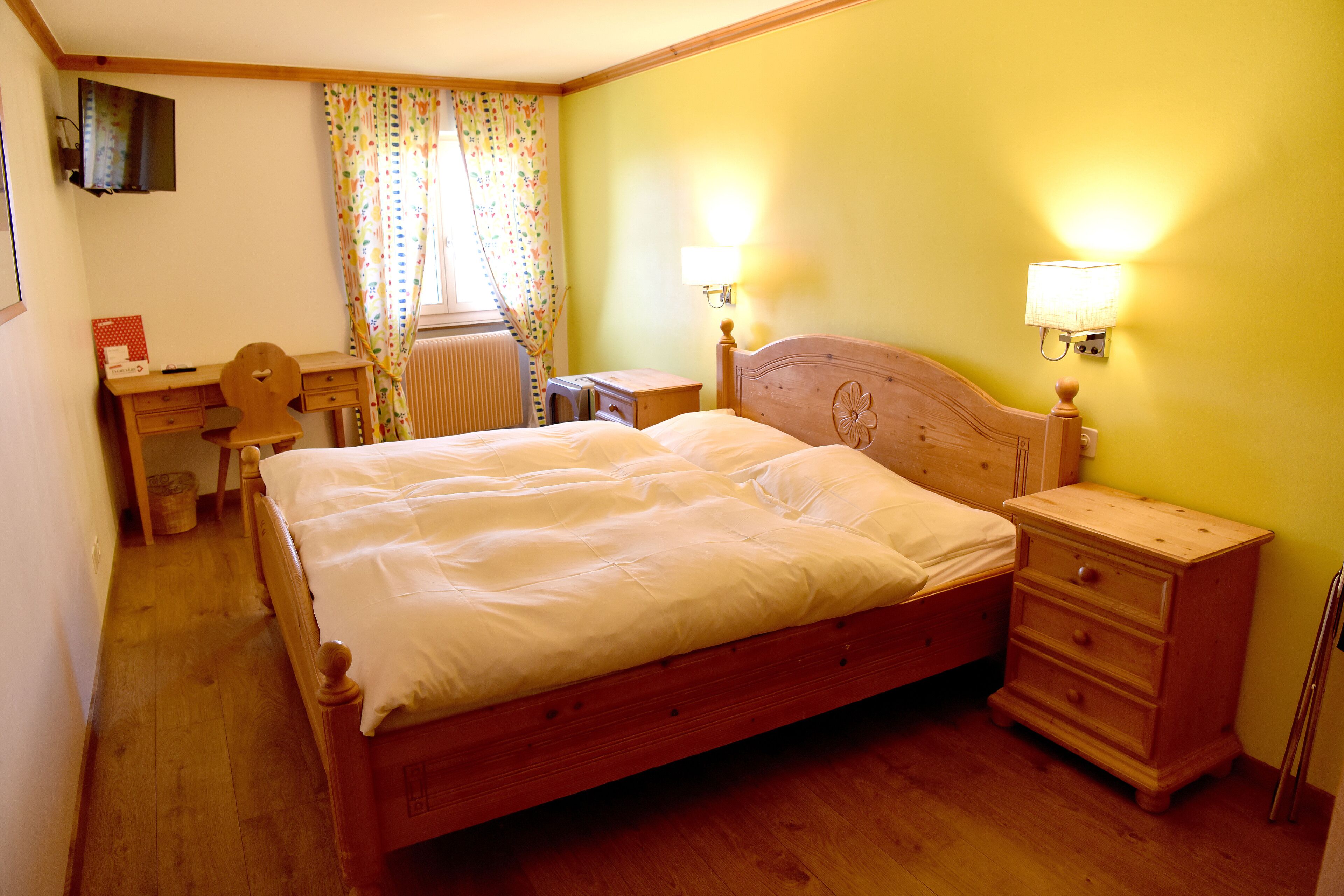 A bedroom with a wooden bed, a desk, a chair, and a nightstand.