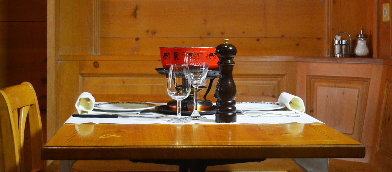A wooden dining table set with plates, glasses, and a pepper mill.
