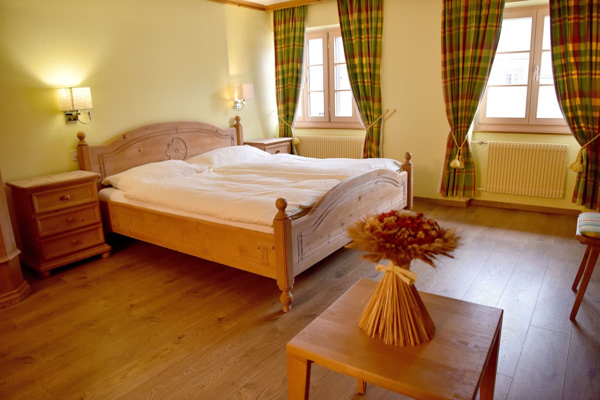 A wooden bed with a headboard, a bedside table, a lamp, and a vase with flowers on a small table.