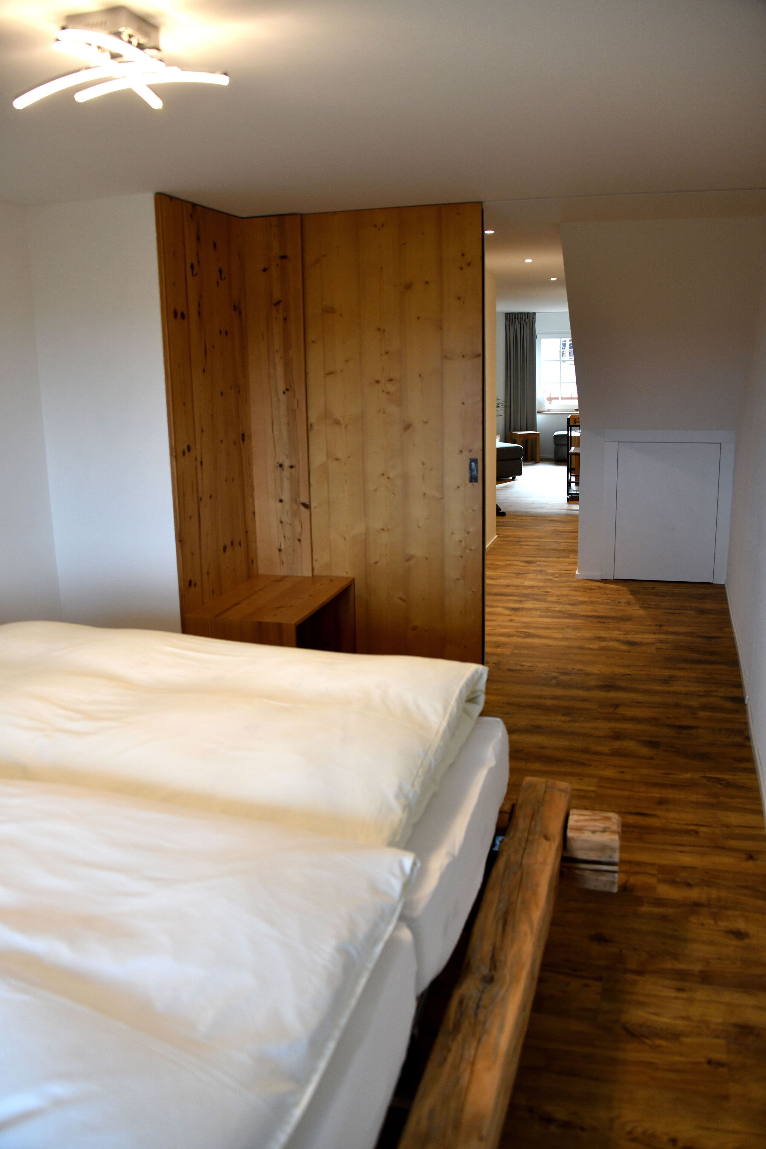 A bedroom with a wooden wardrobe, a wooden bench, and a wooden bed frame.