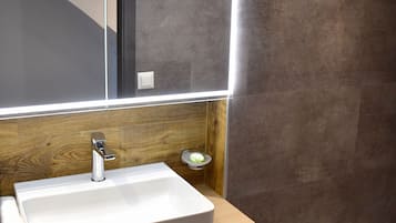 Une salle de bain moderne avec un lavabo blanc, un meuble-lavabo en bois et un grand miroir doté d’un éclairage intégré.