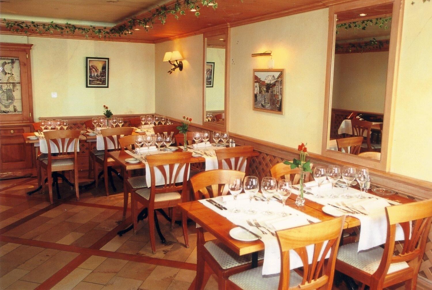 A dining area with multiple tables set for a meal, wooden chairs, and wall-mounted light fixtures.