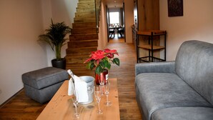 Ein modernes Wohnzimmer mit einer Holztreppe, grauen Sofas, einem Holztisch mit Weingläsern, einer Topfpflanze und einem Essbereich im Hintergrund.