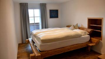 Un dormitorio con una cama de madera, una ventana con cortinas, un cuadro en la pared y una estantería de madera.