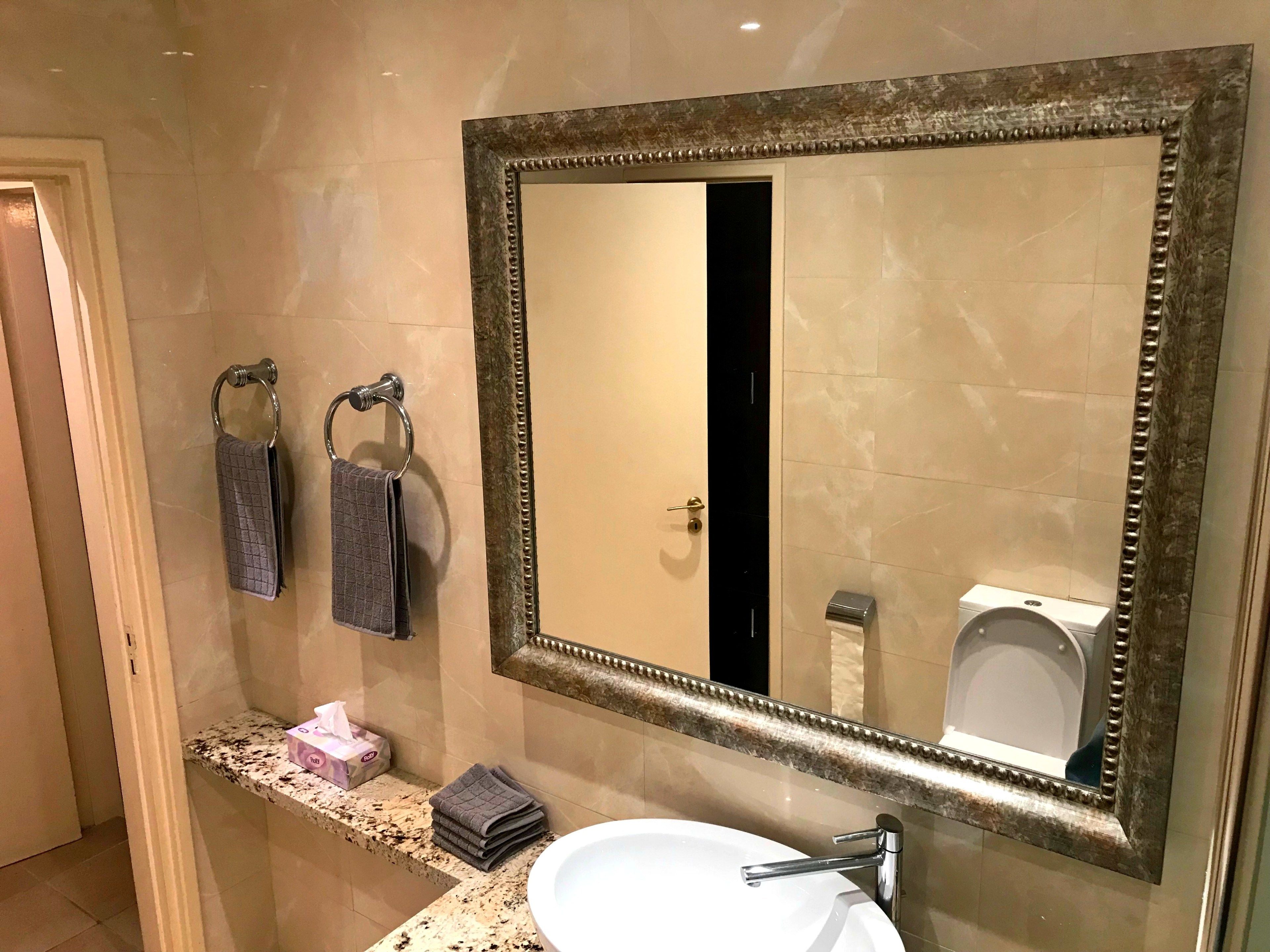 Een badkamer met een grote spiegel, een wastafel en twee handdoeken aan handdoekhouders.