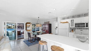 A modern kitchen with white cabinets, a large island, and a dining area with a view of the pool. - Naples Lake House. Bike to Beach. Pet Friendly (Naples)