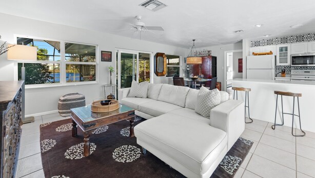 A modern living room with a white sofa, a coffee table, and a kitchen area with white cabinets and a microwave. - Naples Lake House. Bike to Beach. Pet Friendly (Naples)