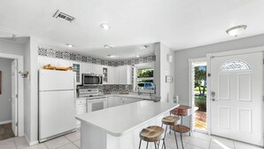 A modern kitchen with white cabinetry, a central island, and bar stools. - Naples Lake House. Bike to Beach. Pet Friendly (Naples)
