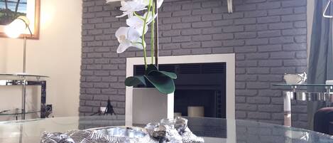 A room with a glass table, a white orchid, and a silver frog sculpture.