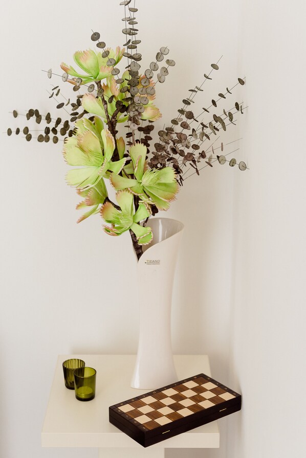 A vase with a floral arrangement on a white table, accompanied by a chessboard and two green glasses.