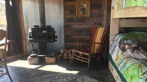 Interior rústico de una cabaña con una cama de madera, un cuadro en la pared y una chimenea.