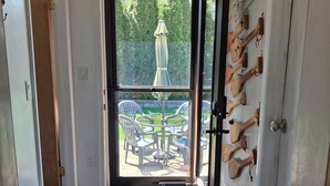 Una puerta que da a un patio exterior con una mesa y sillas, un bate de madera colgado en la pared, y un banco de madera en el interior.