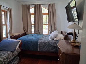 A bedroom with a bed, a bedside table, a lamp, a television, and a window with curtains.