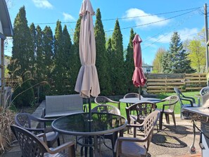 An outdoor patio with round tables and chairs, two umbrellas, and a wooden fence.