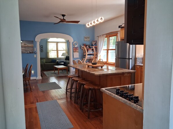 A kitchen with a wooden island, bar stools, a refrigerator, and a dining area with a table and chairs.