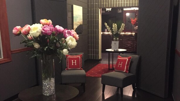 A lobby with a red carpet, two grey armchairs with red cushions, a vase with flowers, and a clock on the wall. - Hamilton Hotel (Williams Lake)