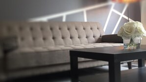 A modern living room with a tufted sofa, a dark coffee table, and a vase with white flowers. - Hamilton Hotel (Williams Lake)
