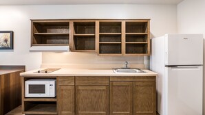 A compact kitchen with wooden cabinets, a built-in microwave, a sink, and a white refrigerator. - WoodSpring Suites Merrillville (Merrillville)