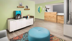 A modern hotel room with a kitchenette, a blue ottoman, and a colorful rug. - WoodSpring Suites Merrillville (Merrillville)