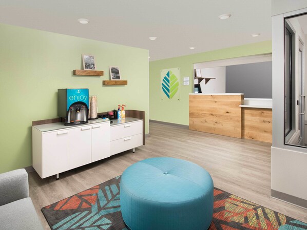 A modern hotel room with a kitchenette, a blue ottoman, and a colorful rug. - WoodSpring Suites Merrillville (Merrillville)