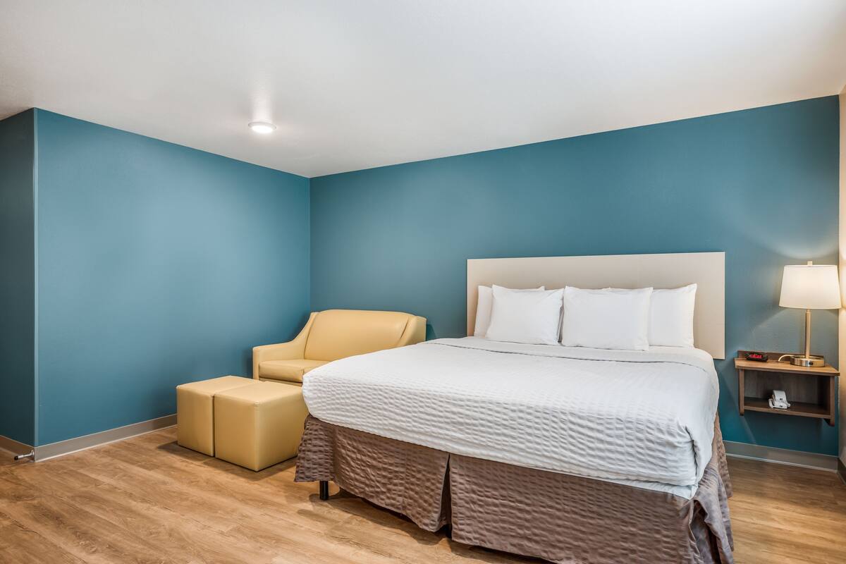 A hotel room with a large bed, a chair, and a bedside table with a lamp.