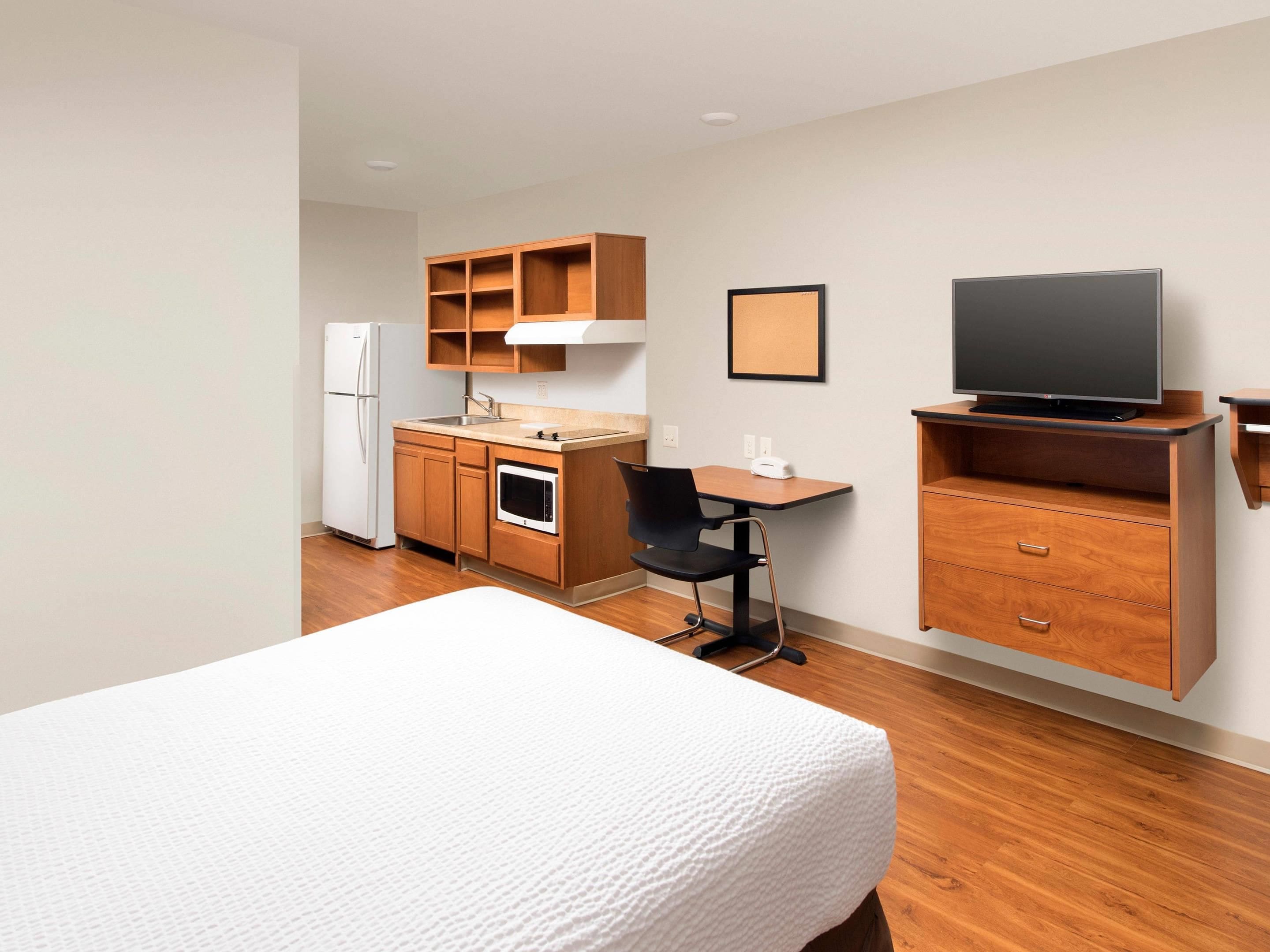 A hotel room with a bed, a desk, a chair, a television, a kitchenette, and a refrigerator.
