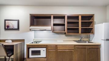 Una cocina compacta con armarios de madera, un microondas, un lavamanos y una silla.