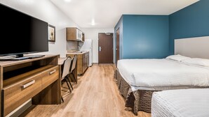 A compact hotel room with a bed, a desk with a computer, a microwave, and a wardrobe. - WoodSpring Suites Merrillville (Merrillville)