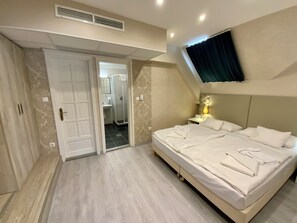 A bedroom with a large bed, a TV mounted on the wall, a shower area, and a door leading to another room. - Bastya Wellness Hotel (Miskolc)
