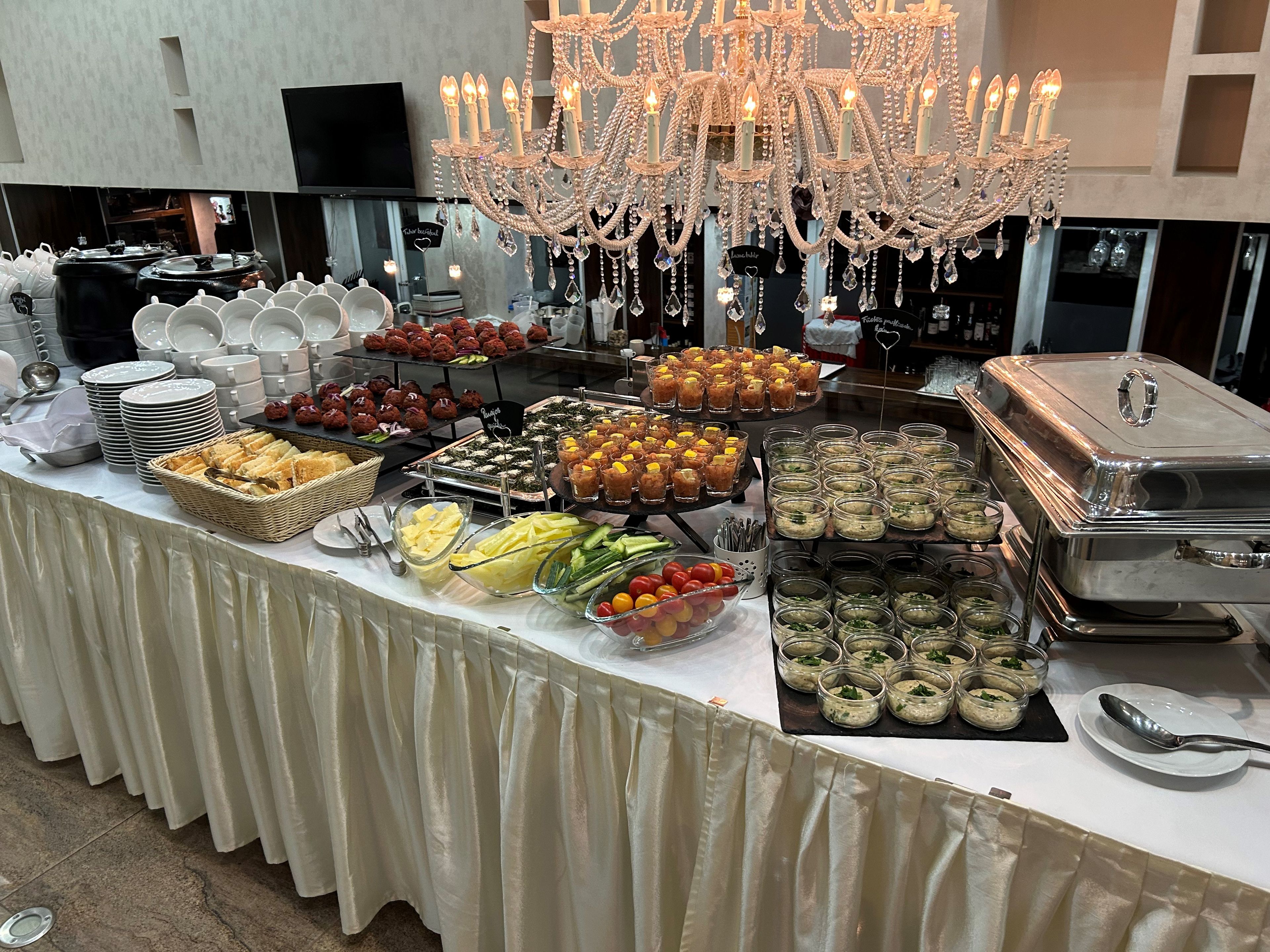 A buffet table with various food items, a chandelier, and a TV in the background.