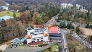 An aerial view of a campus with a swimming pool, parking area, and buildings surrounded by trees. - Bastya Wellness Hotel (Miskolc)