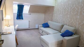 A modern living room with a white sofa, two blue cushions, a white desk with a lamp, and a window with blue curtains.