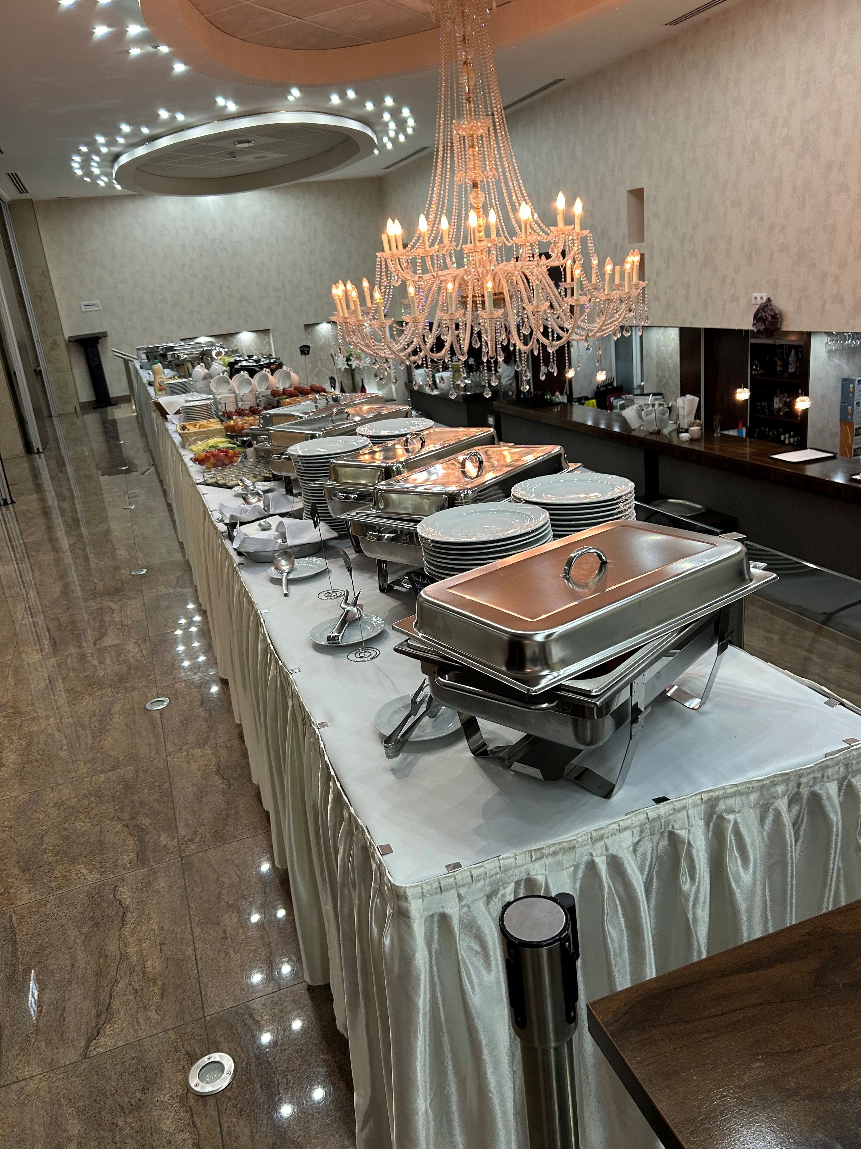 A buffet setup with multiple serving stations, a chandelier, and a long table covered with a white cloth.
