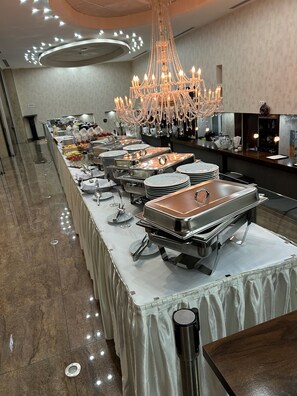 A buffet setup with multiple serving stations, a chandelier, and a long table covered with a white cloth. - Bastya Wellness Hotel (Miskolc)