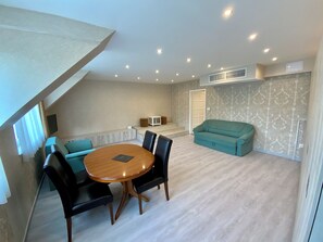 A modern living room with a round wooden table, black chairs, a teal sofa, and a staircase leading to another level. - Bastya Wellness Hotel (Miskolc)