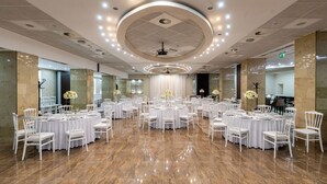 A spacious banquet hall with multiple round tables and white chairs, a polished marble floor, and a modern ceiling design with recessed lighting. - Bastya Wellness Hotel (Miskolc)